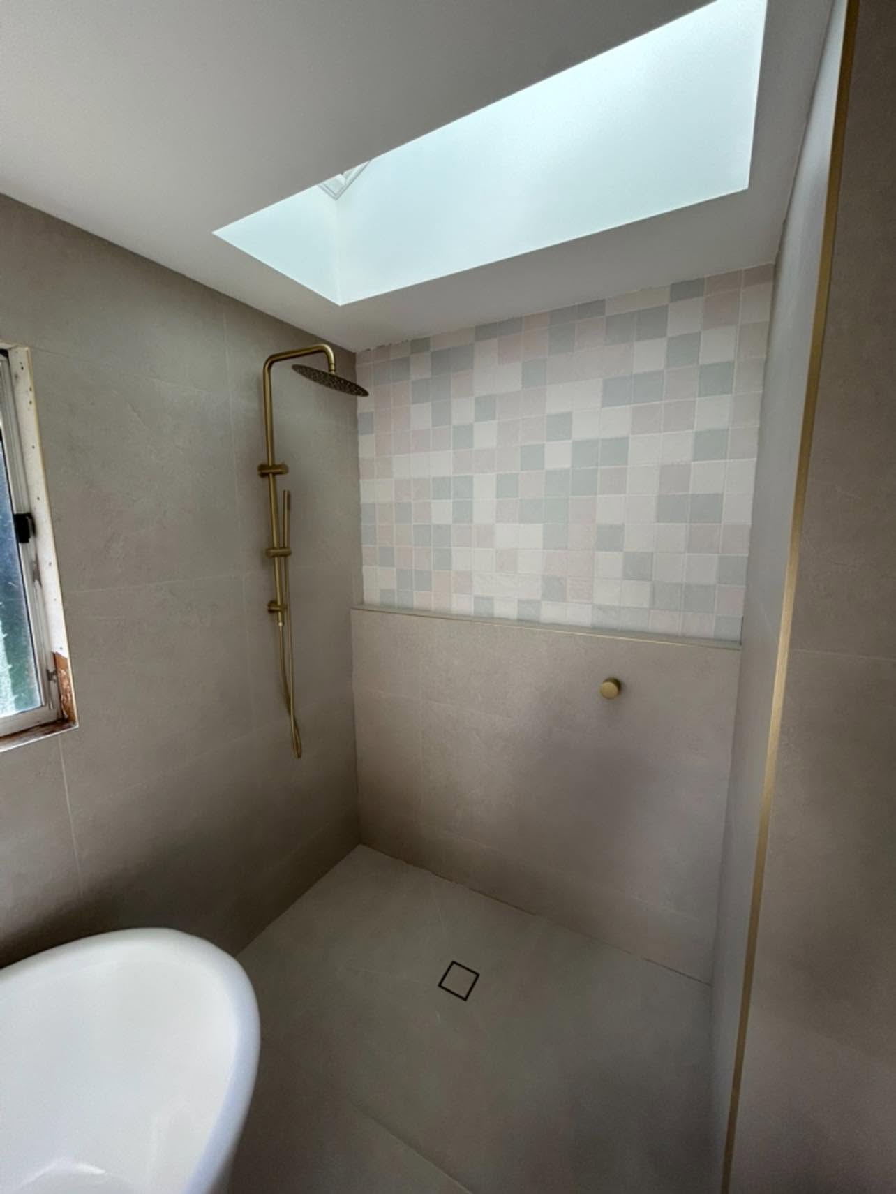 Walk-in shower with brushed brass shower rail, skylight and freestanding bath