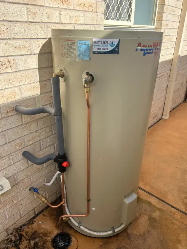 Hot water cylinder with copper pipework installed against a brick wall