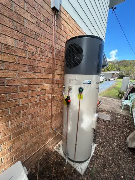 Heat pump hot water system installed beside a brick house
