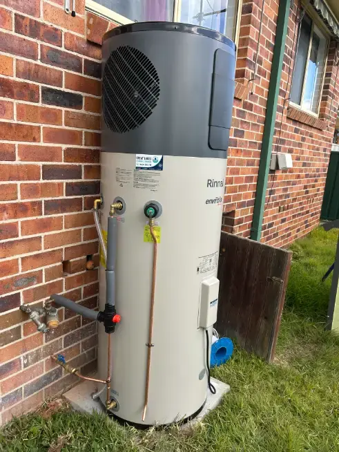 Heat pump hot water unit installed beside a brick house and lawn