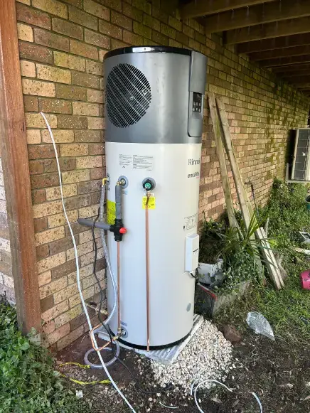 Heat pump hot water unit installed beside a brick house