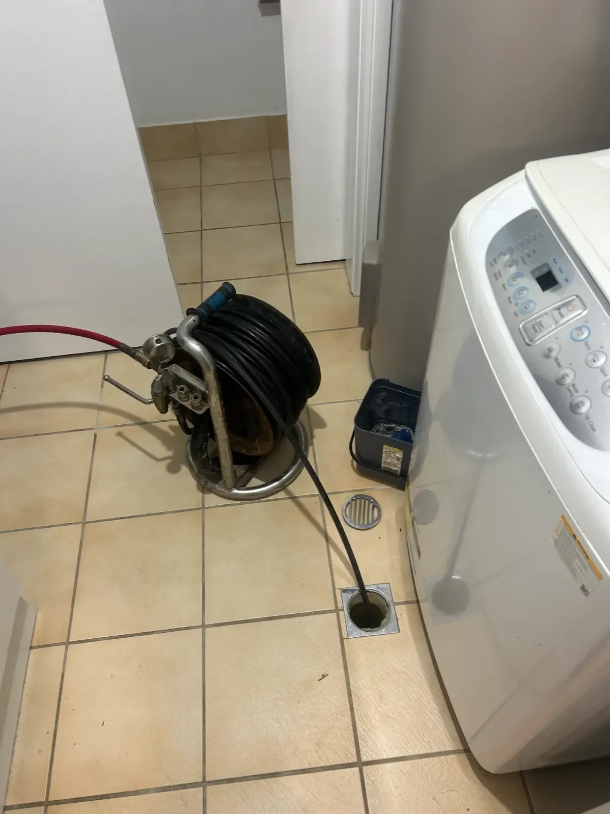 Drain inspection cable and reel positioned beside a laundry floor drain
