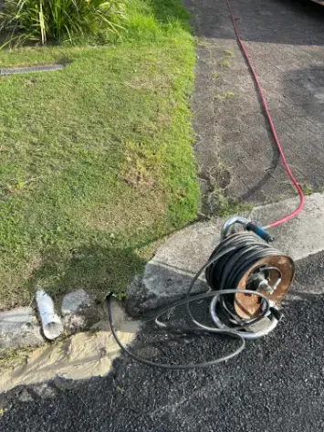 Drain cleaning cable reel and hose set up beside a driveway